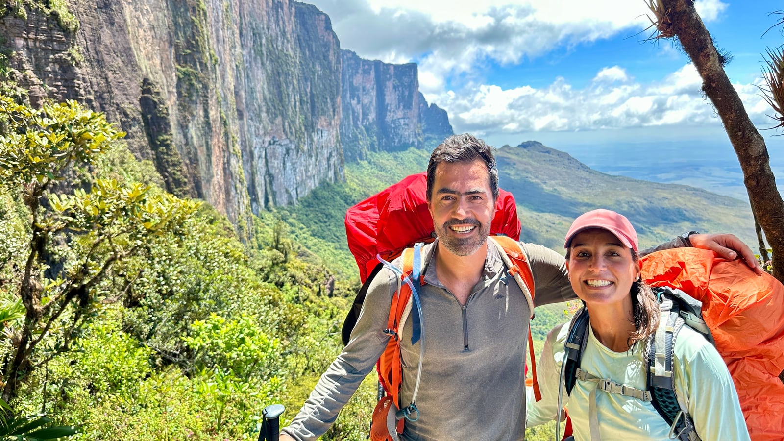 Thaíssa e Julián sorrindo com as mochilas cargueiras nas costas, com a parede do Monte Roraima atrás