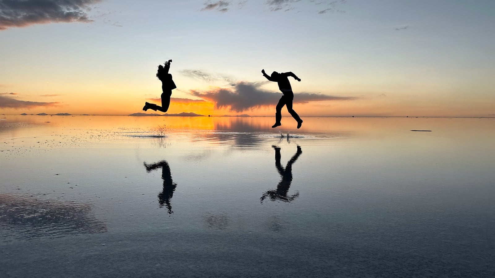O salar de Uyuni virado espelho, com duas silhuetas saltando refletidas na água