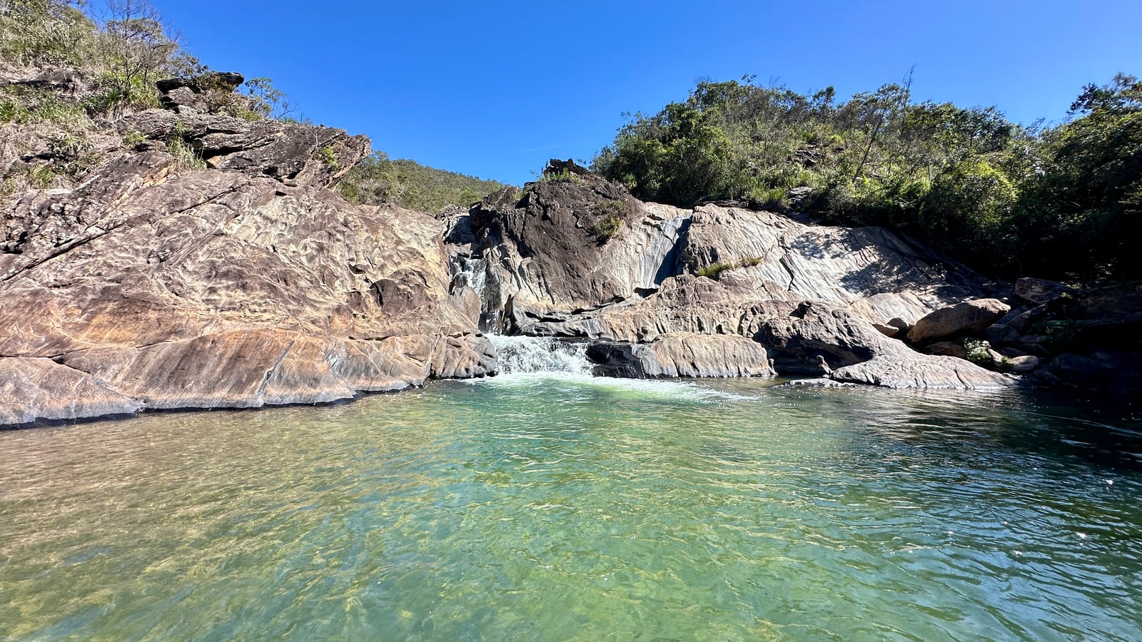 Um poço de água clara entre lajes de pedra, com a serra ao fundo