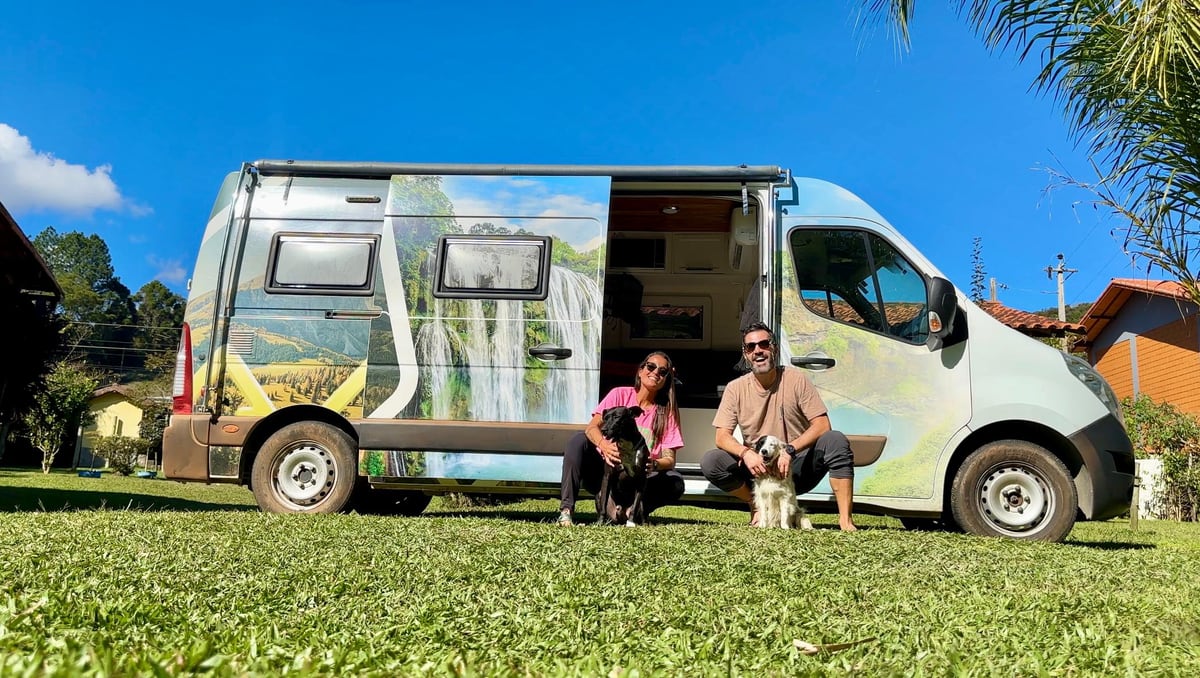Thaíssa, Julián e os dois cachorros sentados na grama, na frente do motorhome alugado
